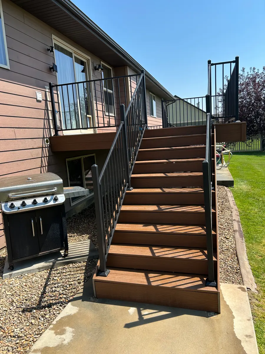Finished composite deck with black metal railing and a shade pergola along the back of a house